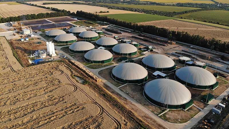 Vista aérea de uma usina de biogás cercada por plantações, com biodigestores cobertos operando para geração de energia renovável.