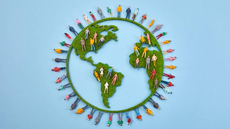 og Ambiental • Representação do planeta Terra com textura de grama e pessoas em miniatura dispostas ao redor, simbolizando diversidade e conexões humanas com a natureza.