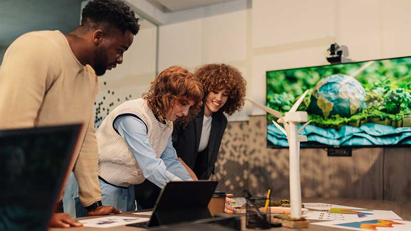 Equipe analisa projeto sustentável com maquete de turbina eólica e tela exibindo o planeta Terra em ambiente colaborativo