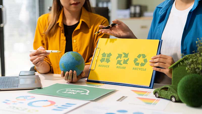Profissionais segurando globo e cartaz com os princípios reduzir, reutilizar e reciclar, em meio a gráficos e documentos de sustentabilidade