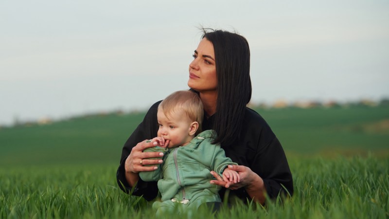 Blog Ambiental • Mãe segurando bebê em um campo verde aberto.