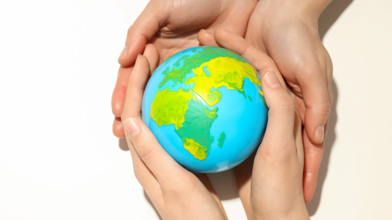 Blog Ambiental • Mãos de adulto envolvendo mãos infantis que seguram um pequeno globo terrestre.