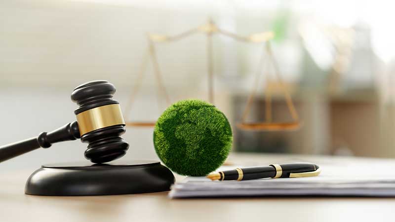 Martelo de juiz, globo verde ecológico e balança da justiça representando regulamentação ambiental corporativa.