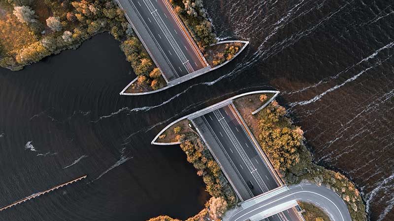 Imagem aérea de uma ponte inacabada sobre um rio, simbolizando falhas na Cooperação Internacional.