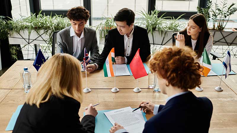 Delegações de diferentes países reunidas em mesa com bandeiras, discutindo acordos de Cooperação Internacional.