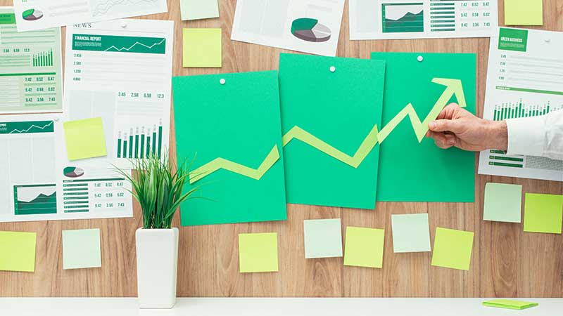 Gráficos verdes de crescimento colados na parede com uma mão apontando para uma seta ascendente, representando exportação sustentável.