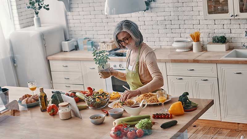 Mulher preparando uma refeição saudável com alimentos frescos e naturais em uma cozinha iluminada e organizada.