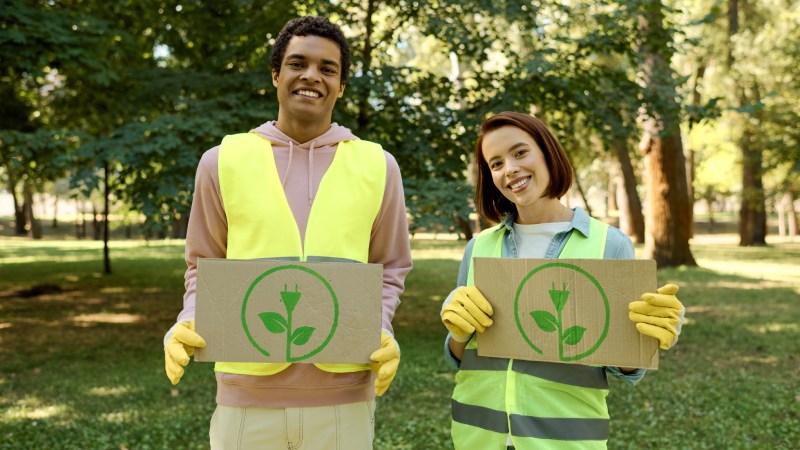 Blog Ambiental • Jovens ambientalistas seguram cartazes com símbolo de sustentabilidade em parque arborizado