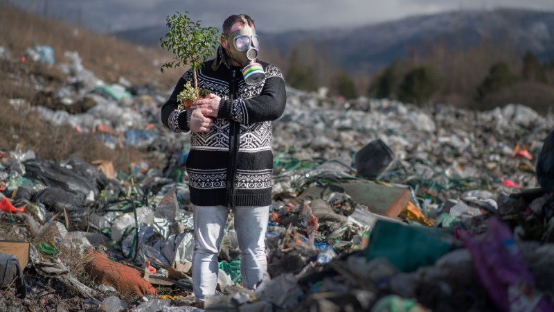 Blog Ambiental • Homem com máscara segurando muda de planta em meio a lixo tóxico