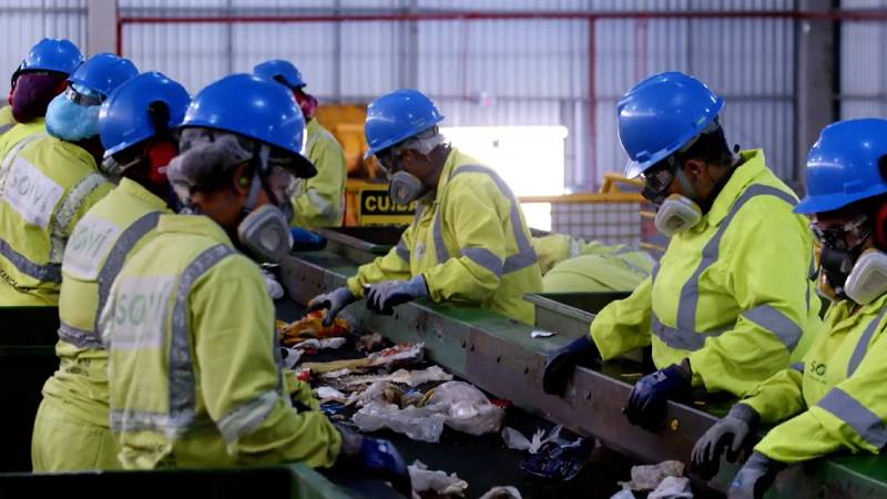 Trabalhadores em linha de triagem de recicláveis, usando EPIs completos — destaque da série O Lixo Também É Seu.
