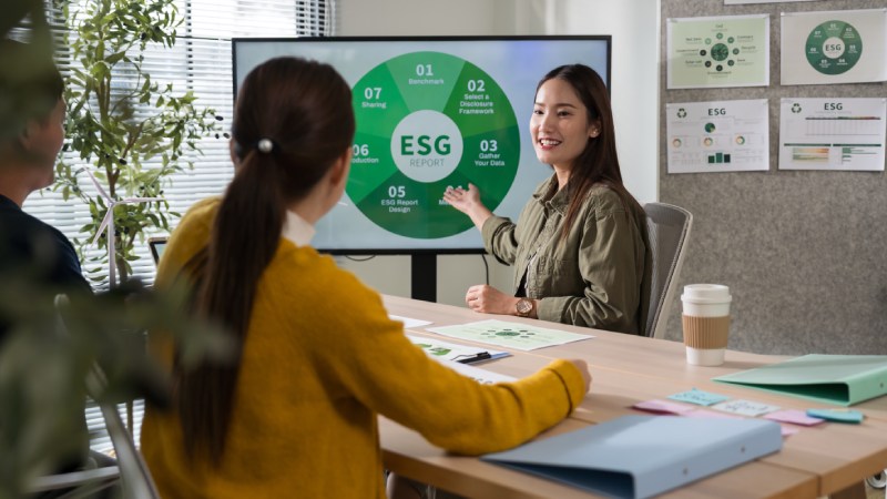 Profissionais reunidos avaliando um painel digital de relatório ESG durante uma apresentação corporativa.