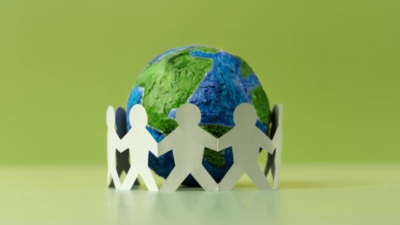 Blog Ambiental • Planeta Terra cercado por figuras humanas de mãos dadas, simbolizando cooperação global e responsabilidade ambiental coletiva