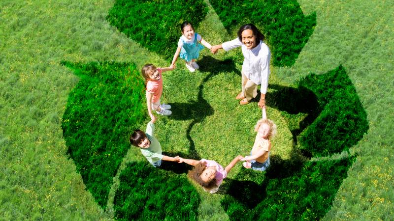 Blog Ambiental • Crianças de mãos dadas formando um símbolo verde no gramado, representando educação ambiental, cooperação e futuro sustentável