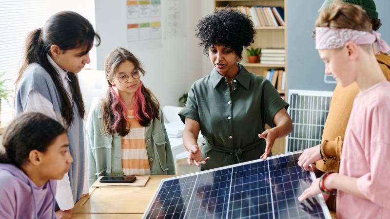 Mulher orientando crianças sobre energia solar e educação ambiental em ambiente educativo.
